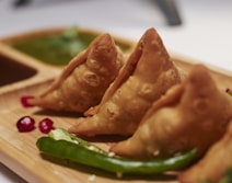 Golden fried samosas served on a wooden board with green chilli